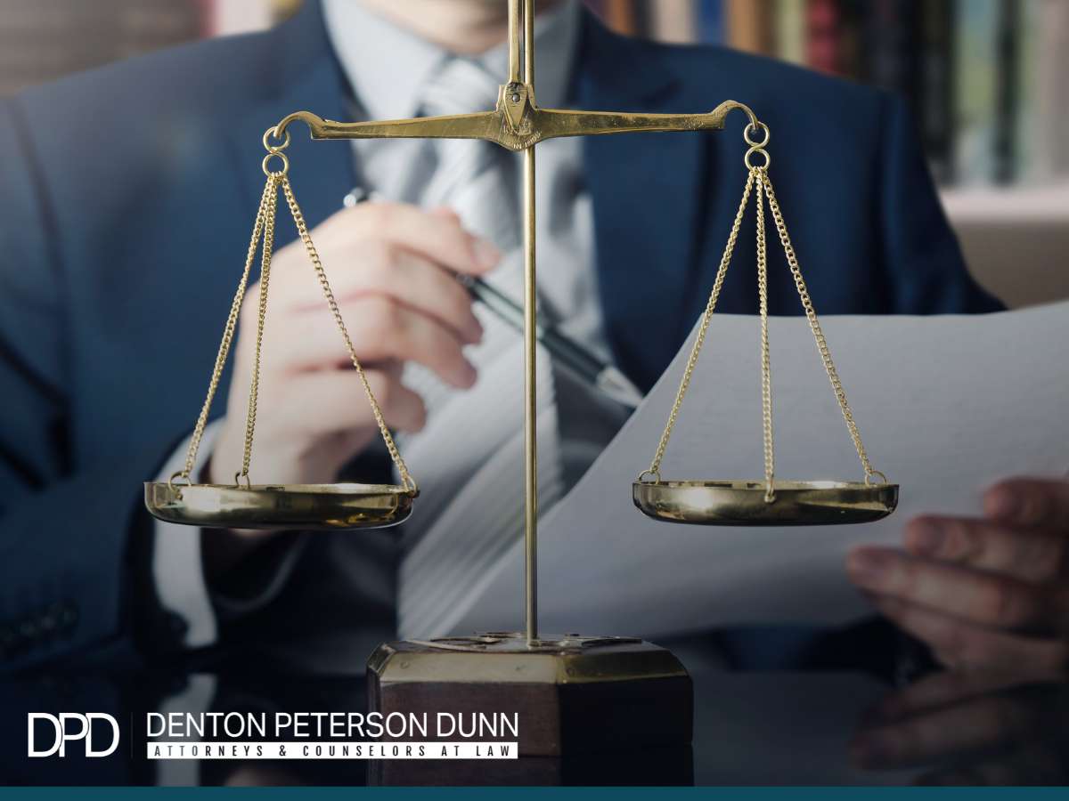 Attorney reviewing documents with a balance scale, symbolizing debt collections law at Denton Peterson Dunn